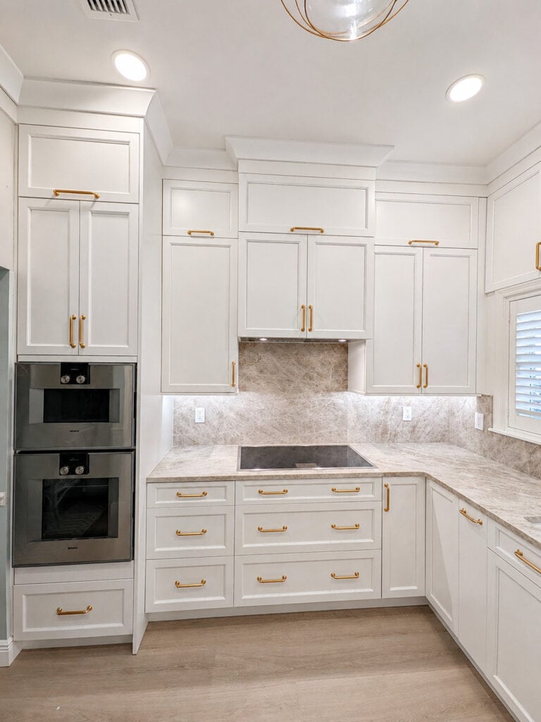 Boca Raton kitchen remodel with white shaker cabinets, brass hardware, double wall ovens, and a Taj Mahal quartzite slab backsplash.