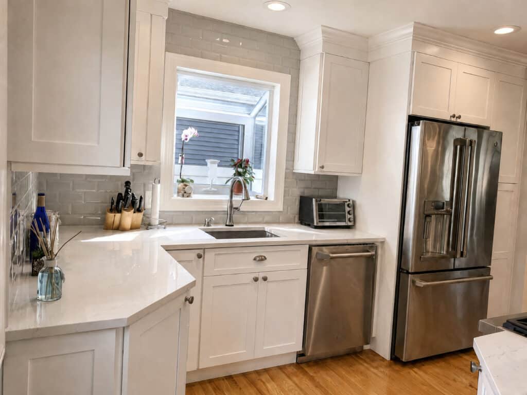 Compact white shaker kitchen with a greenhouse garden window holding orchids above the sink, stainless appliances, and a subway tile backsplash.