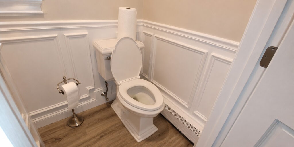 Compact powder room with detailed raised-panel wainscoting, a white toilet, brushed nickel accents, and wood-look plank flooring.