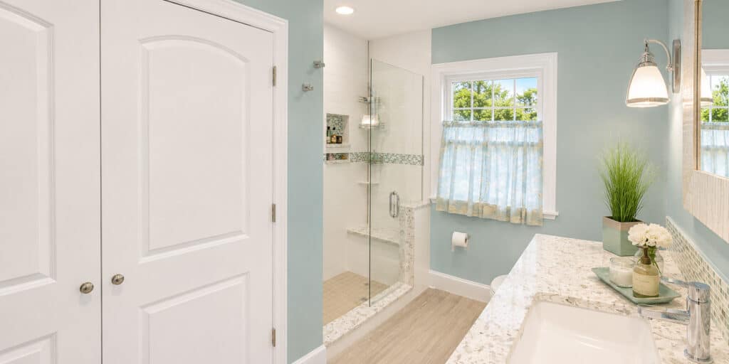 Bright bathroom with a walk-in frameless glass shower, a built-in bench, a terrazzo-look quartz vanity, and a wood-look tile floor.