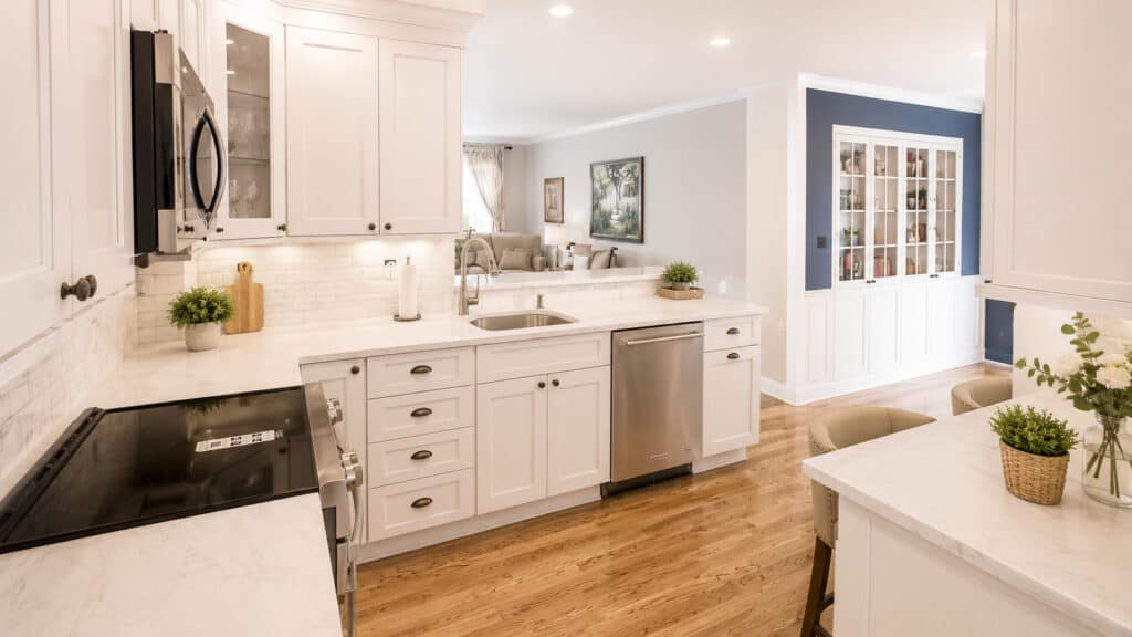 White shaker kitchen with quartz counters, a marble subway tile backsplash, glass-front cabinets, and stainless appliances, open to a living room with a built-in hutch.