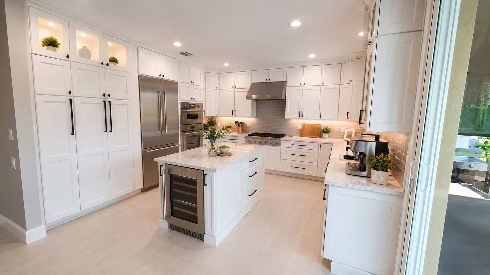Jupiter luxury kitchen remodel with full-height white shaker cabinets, black hardware, a quartz island with a wine fridge, and a glass subway tile backsplash.