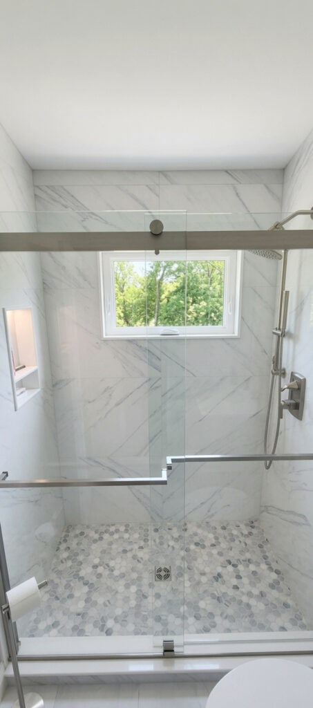Lake Worth shower with large-format marble-look porcelain tile, a hurricane impact awning window, a glass door, and a mosaic tile floor.