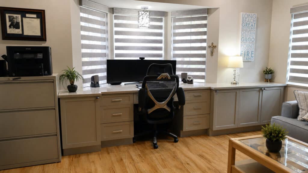 Lake Worth home office with a custom grey built-in desk, quartz top, an ultrawide monitor, and a bay window with layered shades.