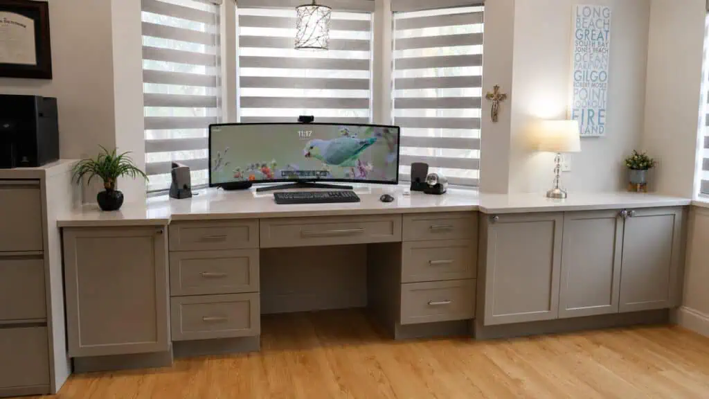 Lake Worth home office with a full-width built-in desk, an ultrawide monitor, storage cabinetry, and a bright bay window.