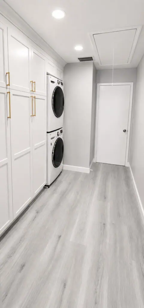Lake Worth laundry room with floor-to-ceiling white shaker cabinets, brass pulls, and a stacked front-load washer and dryer.