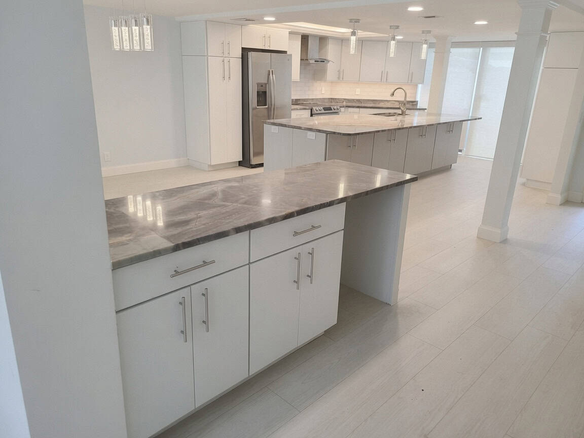 North Palm Beach open-concept kitchen with a large quartz island, white flat-panel cabinets, stainless appliances, and a glass chimney hood.