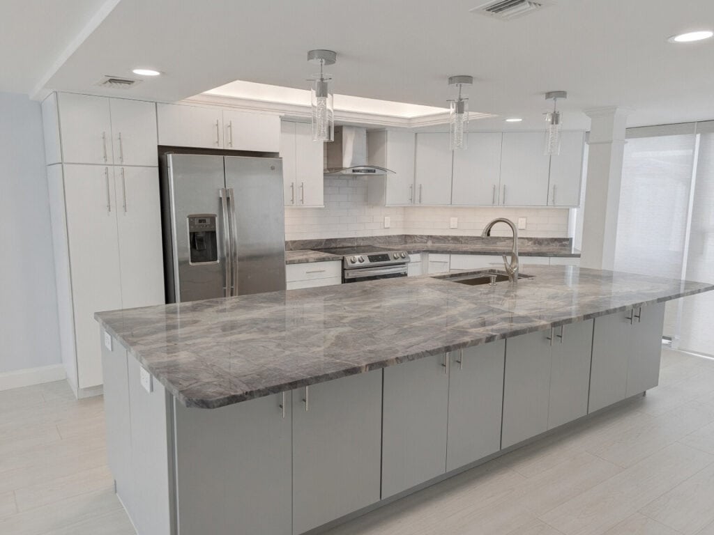 North Palm Beach kitchen with an oversized grey-veined quartz island, white cabinets, stainless appliances, and pendant lighting.