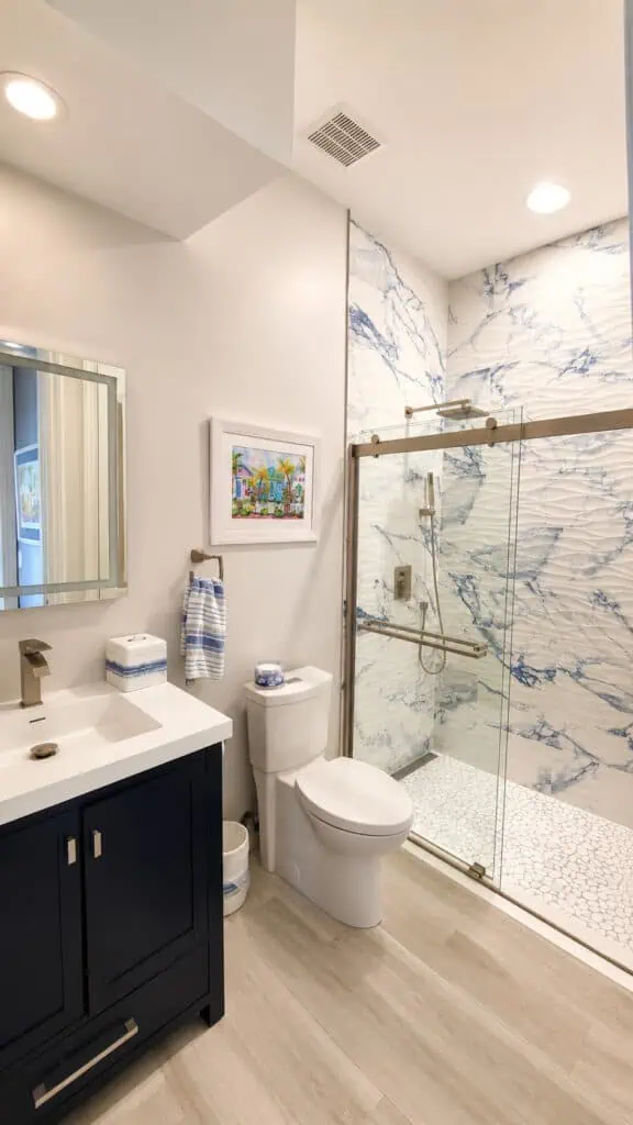 Ocean Ridge coastal bathroom with a navy vanity, a blue-and-white marble-look shower with wavy tile, and nautical accents.