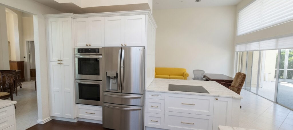 Palm Beach Gardens BallenIsles luxury kitchen with cream raised-panel cabinets, brass hardware, quartzite counters, double wall ovens, and stainless appliances.