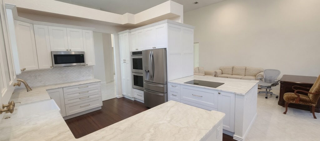 Palm Beach Gardens BallenIsles kitchen with a wrap-around quartzite peninsula, cream cabinets, a farmhouse sink, and an induction cooktop.