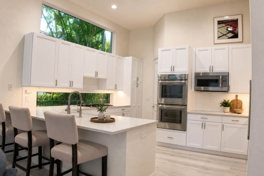 Palm Beach Gardens BallenIsles kitchen with white raised-panel cabinets, a quartz peninsula with seating, stainless appliances, and double wall ovens.
