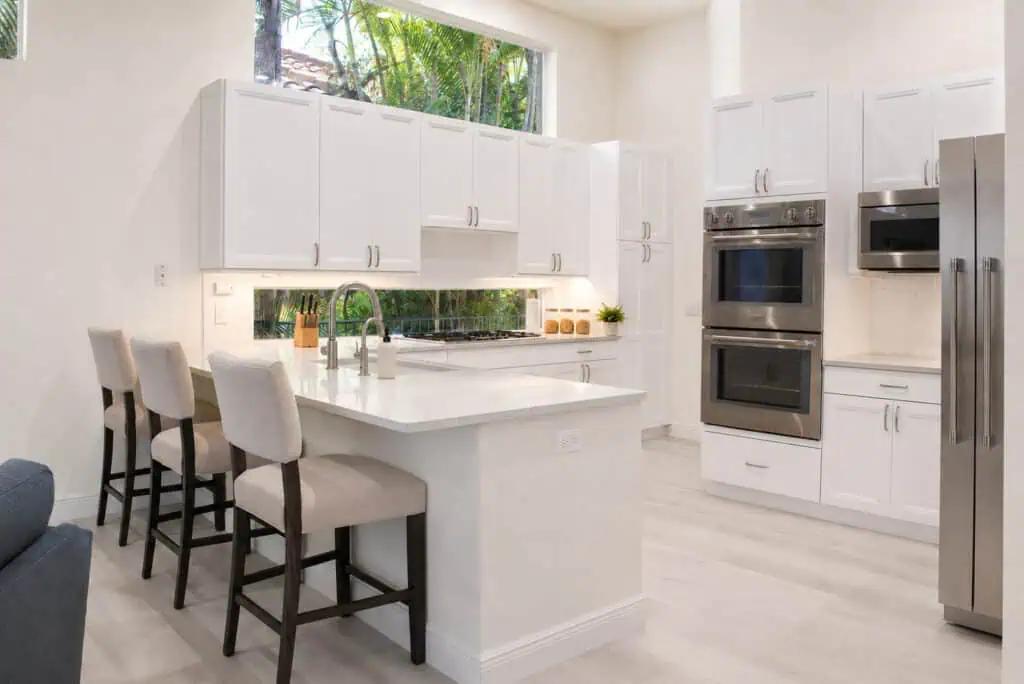 Palm Beach Gardens BallenIsles kitchen with a quartz peninsula and seating, a gas cooktop, double wall ovens, and a built-in refrigerator.