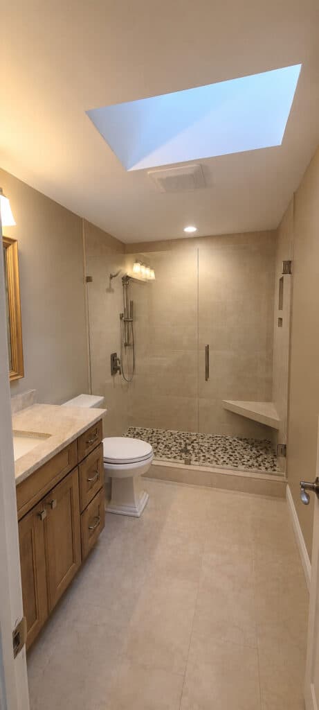PGA National Palm Beach Gardens bathroom with a walk-in shower, pebble mosaic floor, corner bench, a skylight, and a wood vanity with a quartz top.