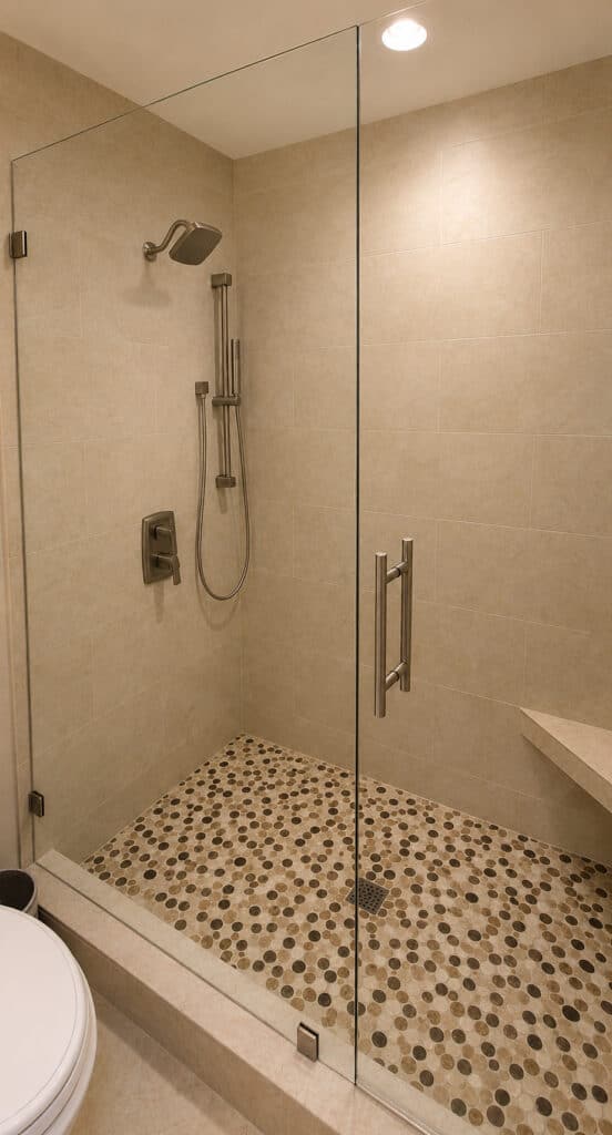 PGA National walk-in shower with stone-look tile, a pebble mosaic floor, a corner bench, and a frameless glass door.
