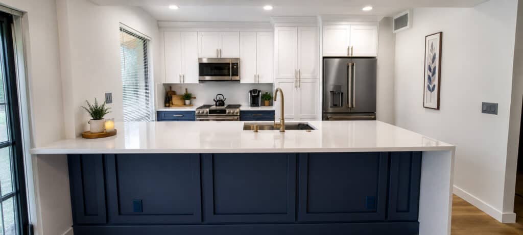 PGA National kitchen with white shaker uppers, navy shaker lowers and island, a white quartz waterfall counter, and brass fixtures.