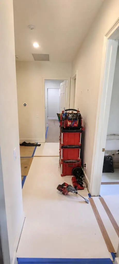 A hallway with kraft-paper floor protection and a modular stacked tool system during a home remodel.