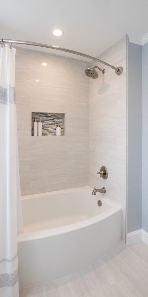 Spa-style tub and shower with a curved-front tub, marble-look large-format tile, a glass mosaic niche, and a curved shower rod.