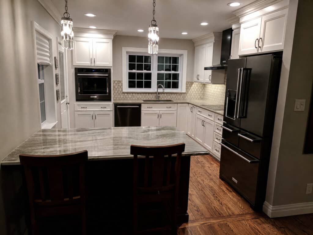 Timeless transitional kitchen with glazed cream cabinets, black stainless appliances, a veined stone island, and crystal pendant lights.