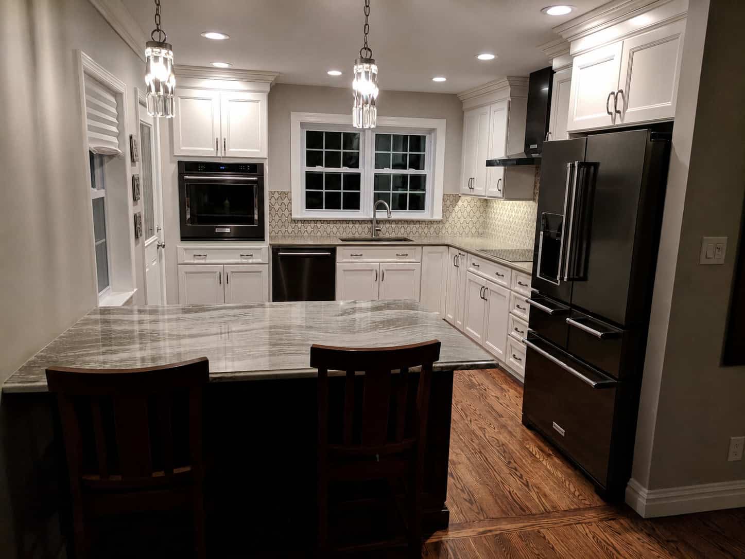 Timeless transitional kitchen with glazed cream cabinets, black stainless appliances, a veined stone island, and crystal pendant lights.