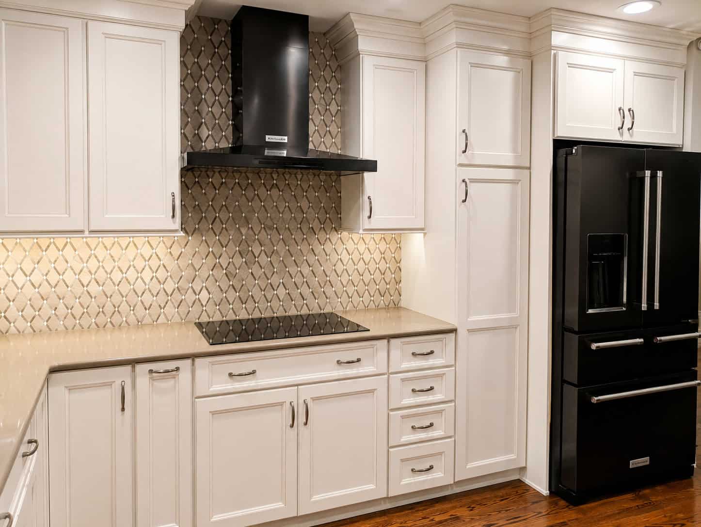 Timeless transitional kitchen range wall with an arabesque mosaic backsplash, a black chimney hood, glazed cream cabinets, and a black stainless refrigerator.
