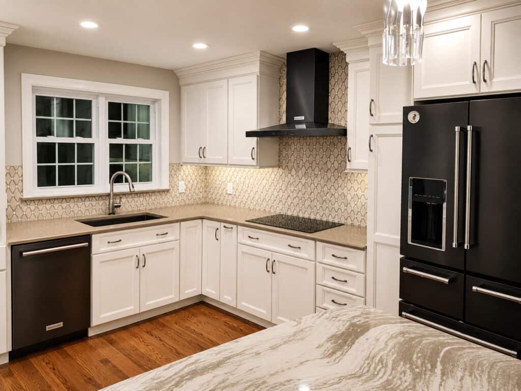 Timeless transitional kitchen with a corner sink, arabesque mosaic backsplash, black stainless appliances, and a crystal pendant.