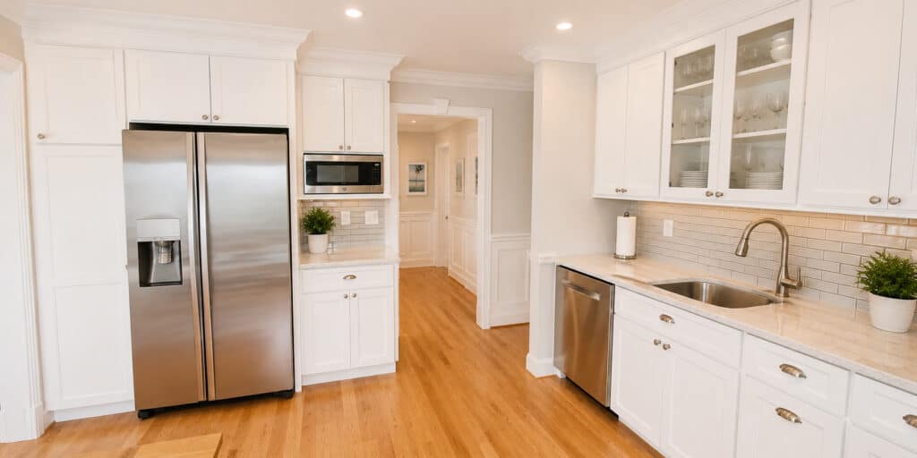 Transitional coastal kitchen with white shaker cabinets, glass-front uppers, quartz counters, a subway backsplash, and stainless appliances.