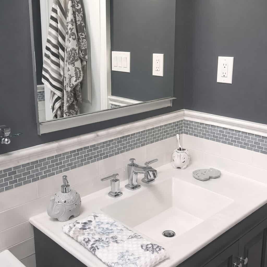 Grey-and-white bathroom vanity with a dark cabinet, quartz top, chrome faucet, white subway tile, and a grey glass mosaic accent band.