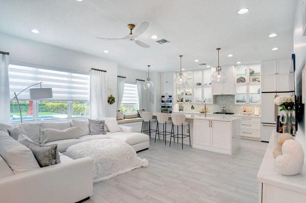 Open-concept Palm Beach County kitchen with a white quartz island opening to a living room, with glass pendants and grey wood-look floors.