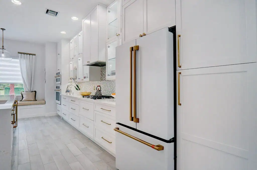 Palm Beach County kitchen with white shaker cabinets, brass pulls, a white French-door refrigerator with brass handles, and a pearl mosaic backsplash.