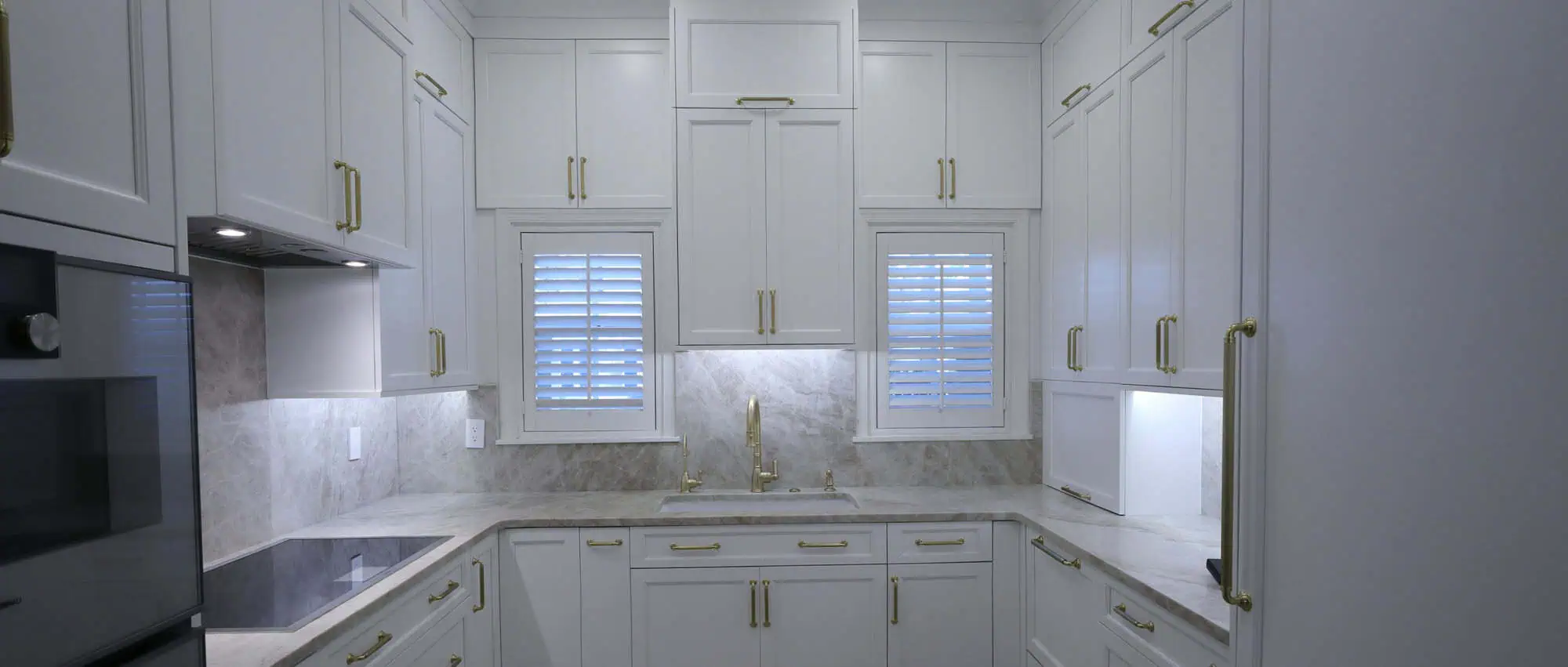 Boca Raton kitchen remodel with white cabinetry, brass hardware, Taj Mahal quartzite countertops and a full-height quartzite backsplash, plantation shutters over the sink and a panel-front refrigerator