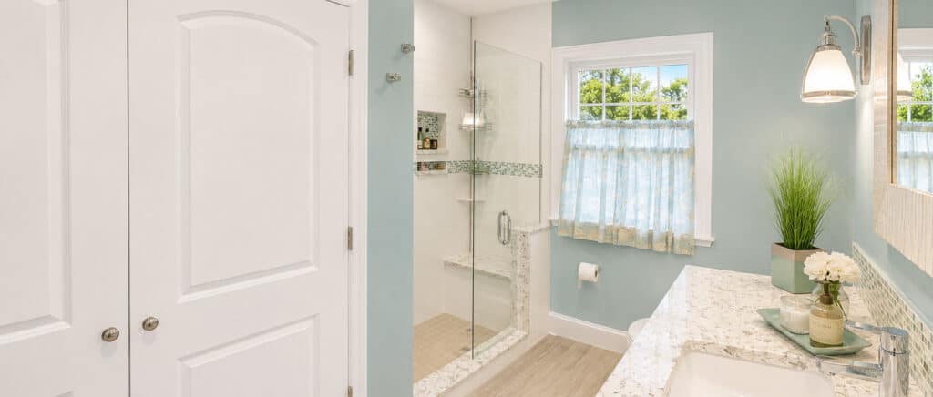 Bathroom remodel with a frameless glass walk-in shower in white subway tile with a glass-mosaic accent band and a built-in bench, beside a speckled stone-look vanity top