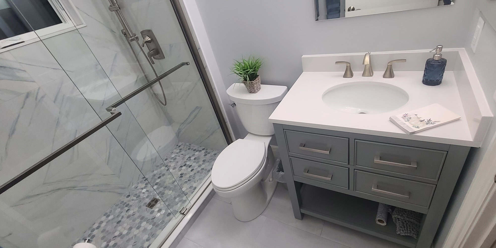 Lake Worth bathroom addition with a grey shaker vanity, a white stone-look countertop, a sliding glass shower door, marble-look large-format wall tile and a blue-grey hex mosaic shower floor