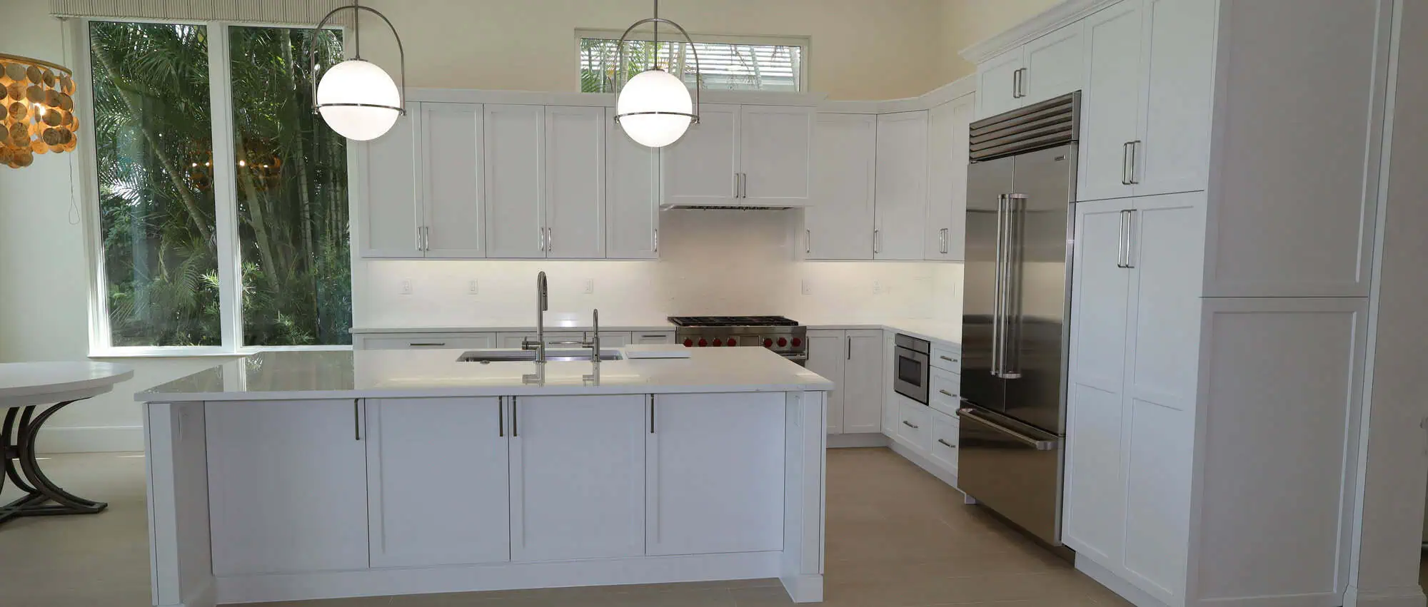 Kitchen remodel in the Mirasol community of Palm Beach Gardens with white shaker cabinets, a quartz-topped island and globe pendant lighting